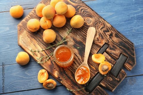 Jar and spoon with sweet apricot jam on wooden board