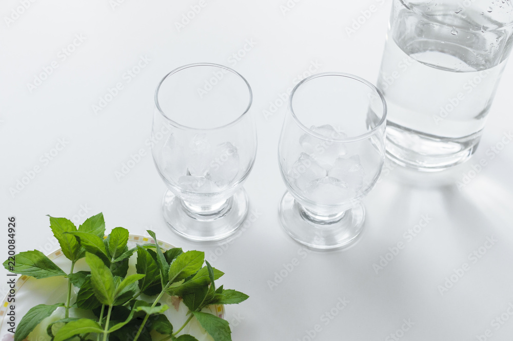 Two glasses with ice cubes, bottle of water and fresh green mint on a plate.