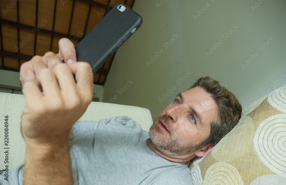 Fototapeta premium lifestyle indoors portrait of young happy and attractive man at home sofa couch using internet social media app on mobile phone networking relaxed