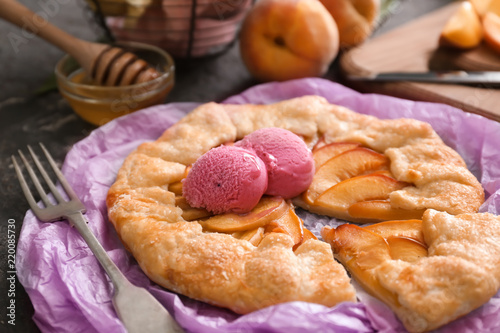 Parchment with delicious peach galette and ice-cream on dark table photo