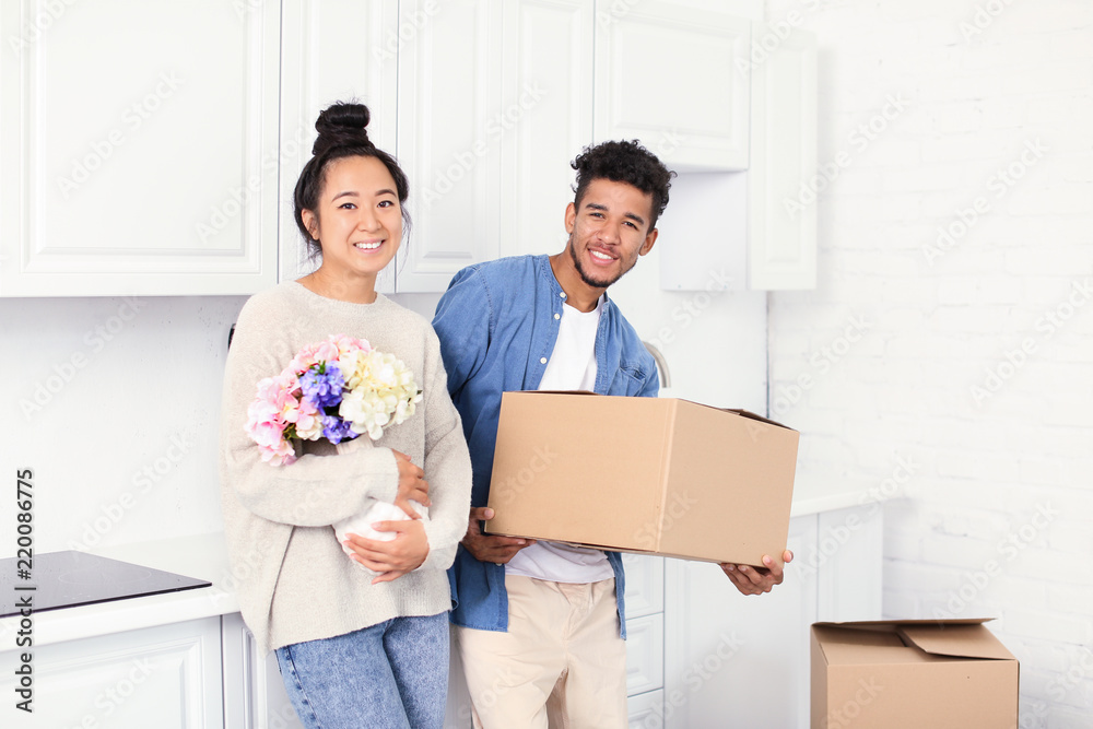 Happy interracial couple unpacking box in kitchen. Moving into new house Happy interracial couple unpacking box in kitchen. Moving into new house
