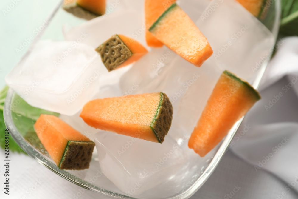 Glass bowl with pieces of melon and ice cubes on table, closeup