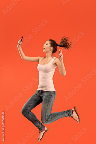 Jump of young woman over blue studio background using laptop or tablet gadget while jumping. Runnin girl in motion or movement. Human emotions and facial expressions concept. Gadget in modern life
