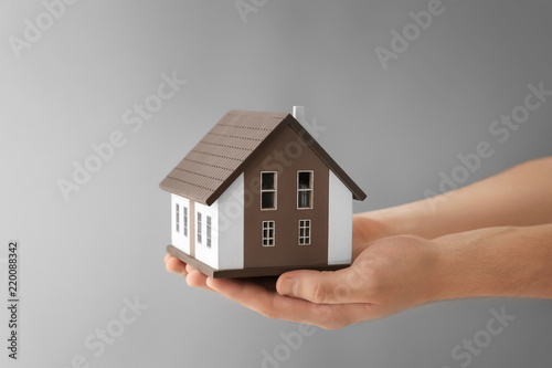 Man holding house model on grey background. Mortgage concept