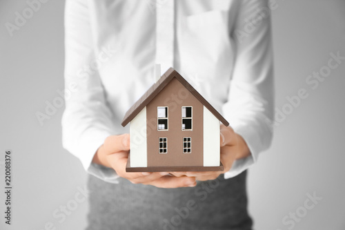 Real estate agent with house model on light background