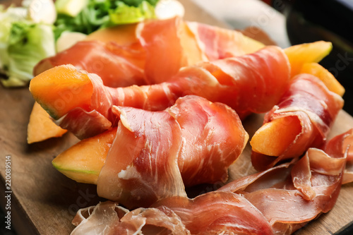 Delicious melon wrapped in prosciutto on wooden board, closeup