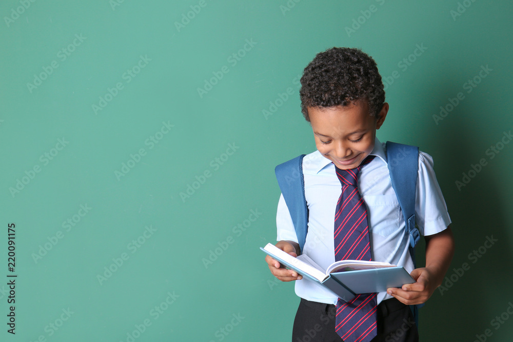 Cute African-American schoolboy reading book on color background Cute African-American schoolboy reading book on color background