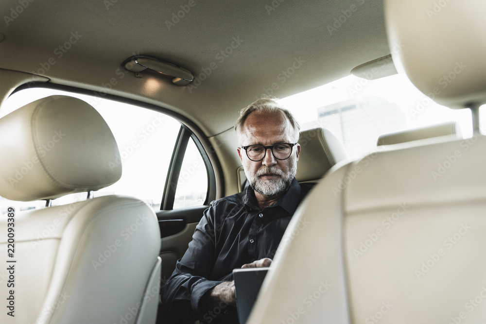 Mature businessman sitting on backseat in car, using digital tablet Mature businessman sitting on backseat in car, using digital tablet