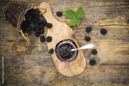 Glass of blackberry jelly and blackberries on wood photo
