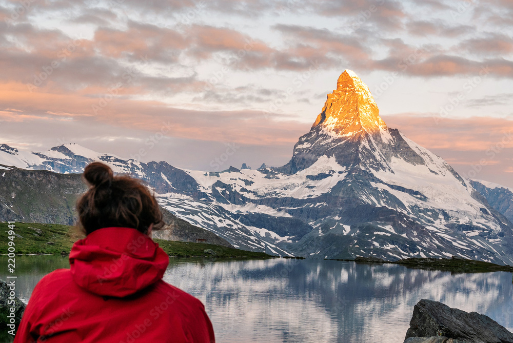Obraz premium Morning shot of the golden Matterhorn (Monte Cervino, Mont Cervin) pyramid and blue Stellisee lake. Female tourist enjoying view of early morning Matterhorn mountain is Valais Alps, Switzerland.