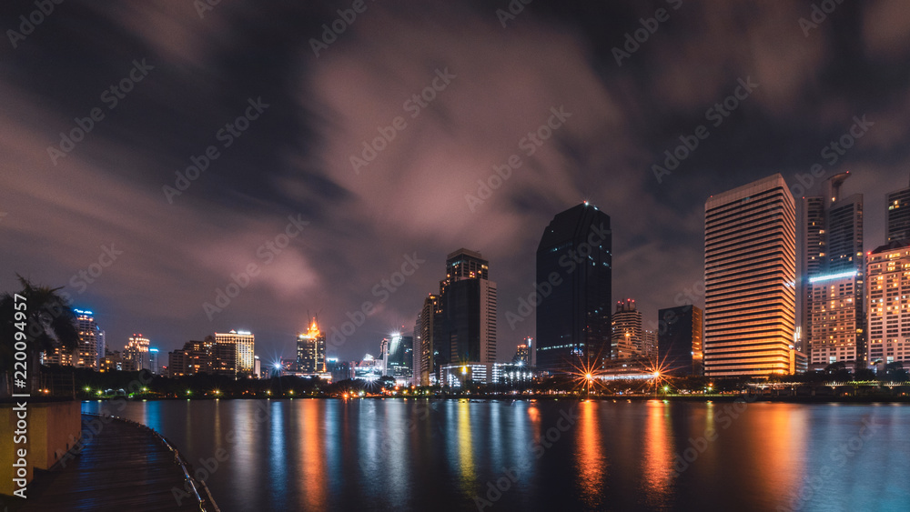 Obraz premium Duże miasto w życiu nocnym z odbiciem fali wody. Technika długiego czasu ekspozycji. Panorama krajobrazu. Koncepcja miasta i urbanistyki. Krajobraz i motyw atrakcji.