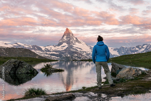 Morning shot of the golden Matterhorn (Monte Cervino, Mont Cervin) pyramid and  blue Stellisee lake. Female tourist enjoying view of early morning Matterhorn mountain is Valais Alps, Switzerland.
