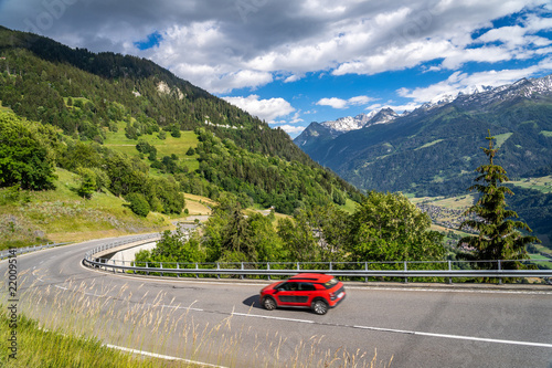 Red car on a road through switzerland alps. Curvy road in mountains. Travelin...
