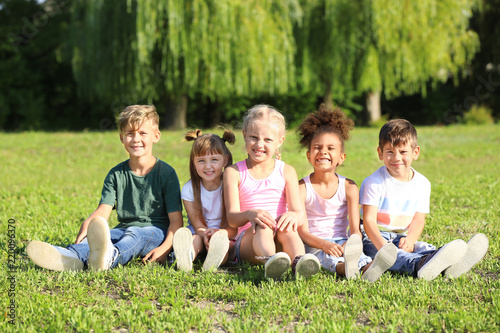 Cute little children sitting on green grass outdoors © Pixel-Shot