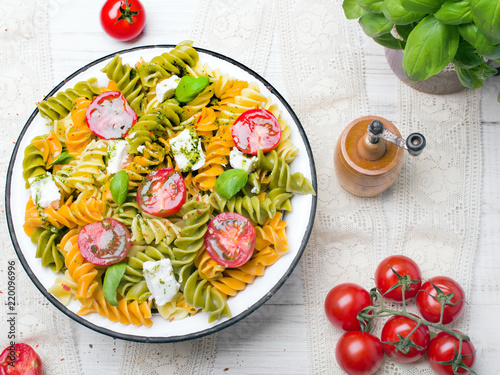 Italian food - Salad with colorful pasta, cherry tomatoes, feta cheese and fresh basil on white wooden background
