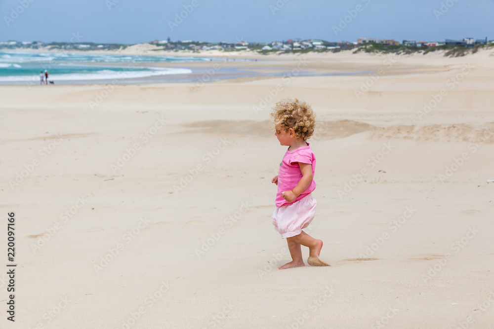 A small toddler walks and plays on the beach, St Francis, South Africa.