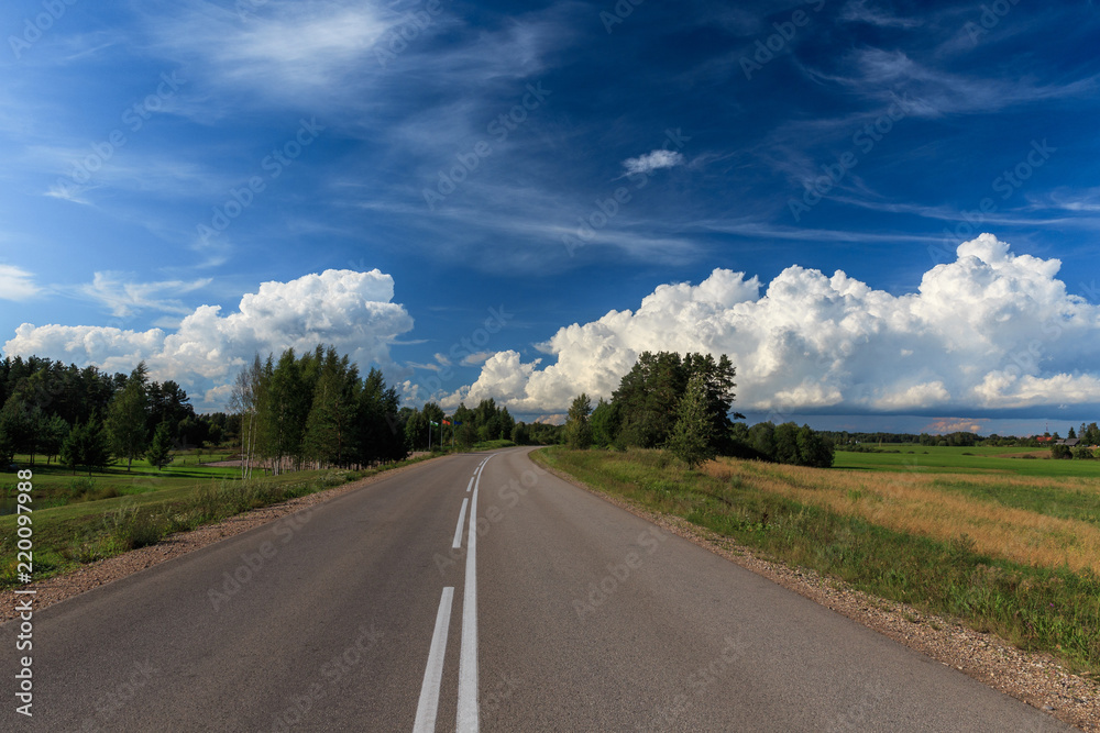 Road up hill with green grass field under white clouds and blue sky in summer day. Latgale. Latvia