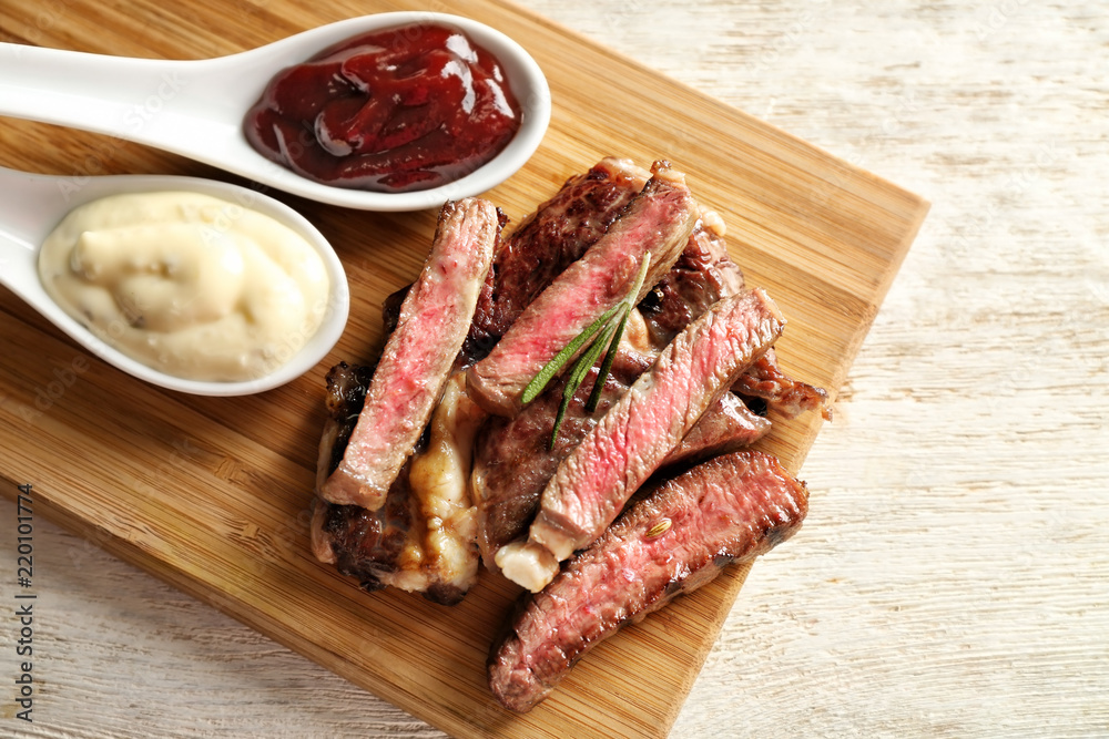 Spoons with sauces and cut grilled steak on wooden board Spoons with sauces and cut grilled steak on wooden board
