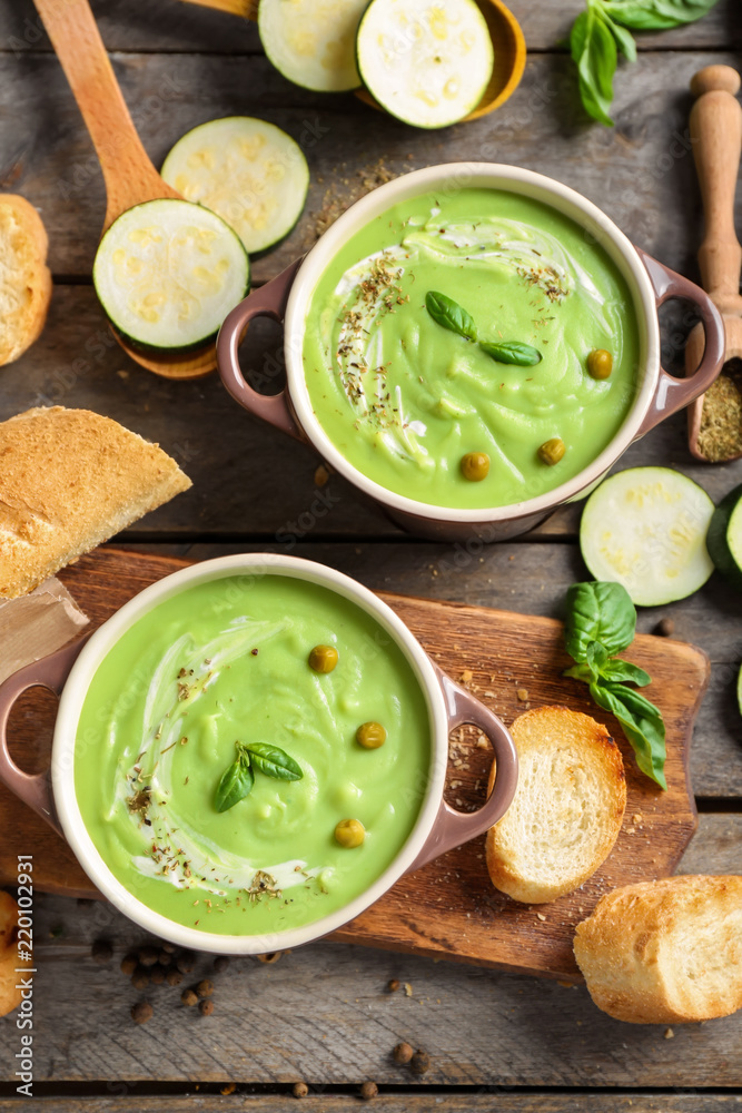 Tasty zucchini soup in saucepans on wooden table