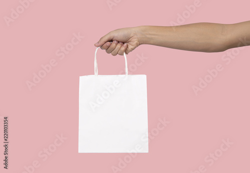 Hand holding blank white paper bag for mockup template advertising and branding isolated on pink background.
