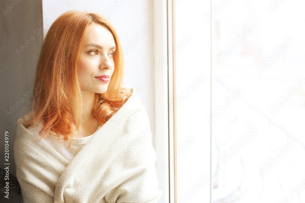 Beautiful redhead young woman with red lipstick on lips sitting by the window of coffee shop, wearing winter autumn season white knitted sweater & big loose scarf on shoulders. Background, close up. Beautiful redhead young woman with red lipstick on lips sitting by the window of coffee shop, wearing winter autumn season white knitted sweater & big loose scarf on shoulders. Background, close up.