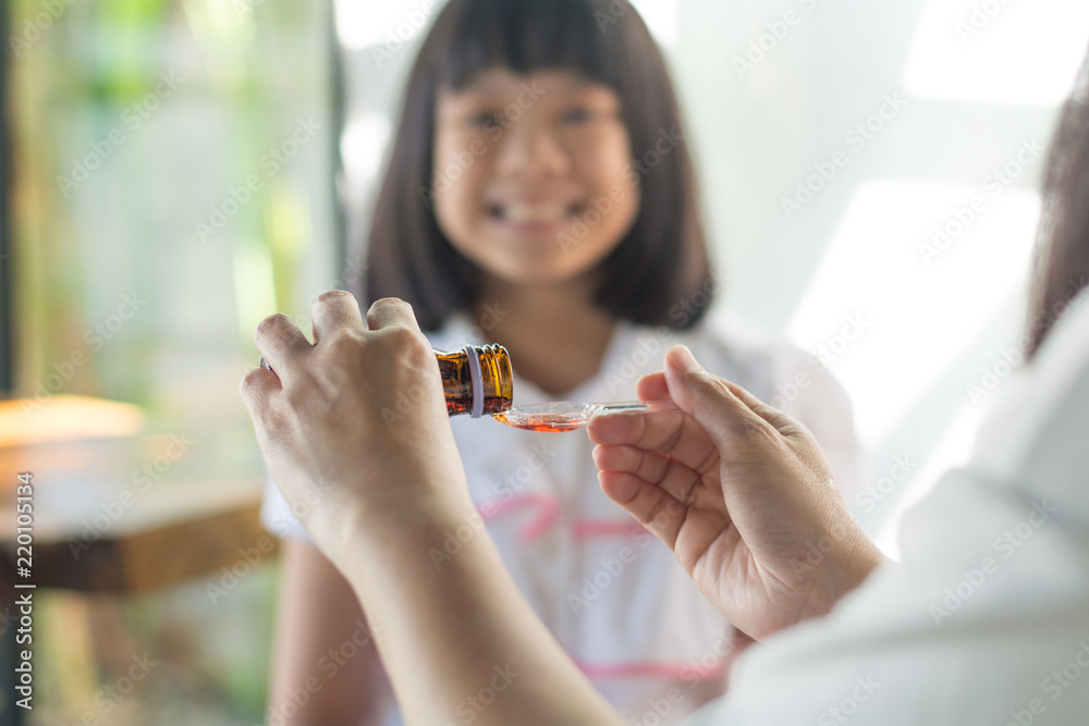 Happy Asia little child girl smiling want to take medicine form mother. Asian kid female waiting to eat drug. Hands of mom pouring cough syrup medicine into clear spoon to daughter. Happy Asia little child girl smiling want to take medicine form mother. Asian kid female waiting to eat drug. Hands of mom pouring cough syrup medicine into clear spoon to daughter.
