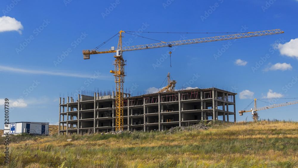 Standard-type apartment building. Kazakhstan (Ust-Kamenogorsk). Construction cranes. High-rise building. Construction site. Building under construction. Steppe