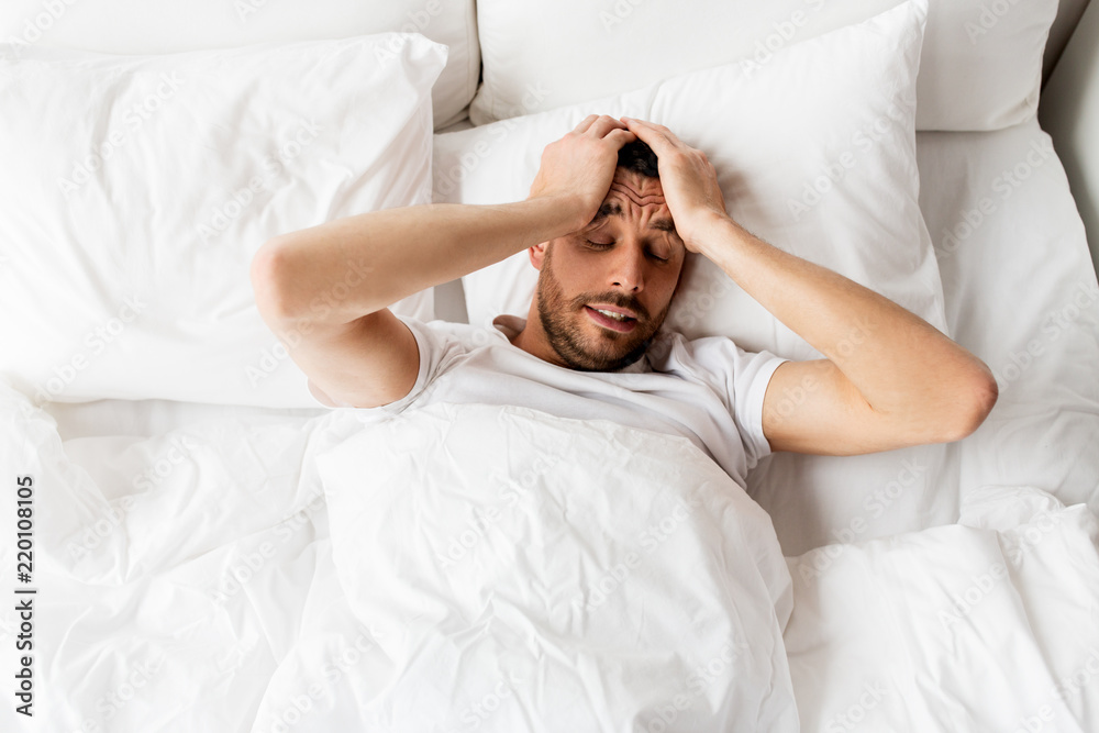 people, bedtime and rest concept - man lying in bed at home suffering from headache or hangover people, bedtime and rest concept - man lying in bed at home suffering from headache or hangover