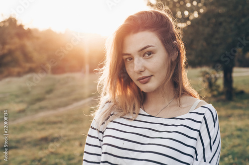 Young woman relaxing in summer sunset sky. Portrait of Beautiful Young Woman Backlit at Sunset Outdoors. Soft warm sunny colors.