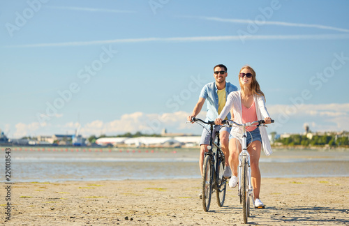 people, leisure and lifestyle concept - happy young couple riding bicycles on beach