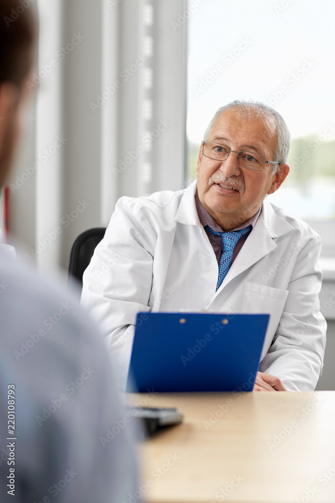 medicine, healthcare and people concept - senior doctor with clipboard talking to young male patient having health problem at hospital