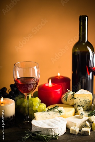 Wine Bottle, Wine Glass, Cheeses, Grape and Lit Candles on the