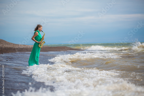 Person playing the saxophone sitting on the rocks in front of a beautiful sea