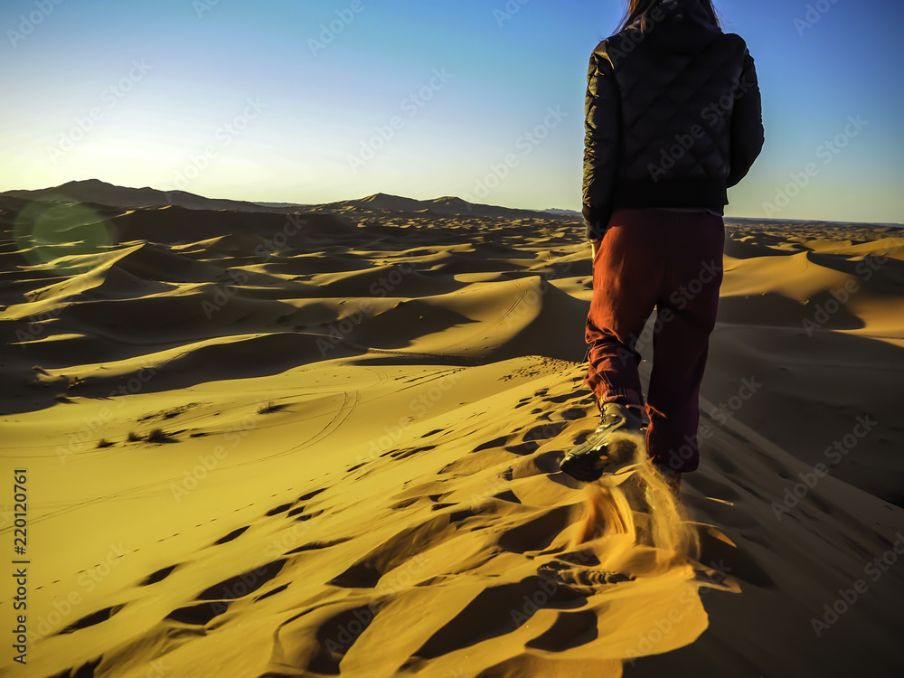 Female traveler enjoying the sunrise on top of a sand dune in Sahara Desert Morocco