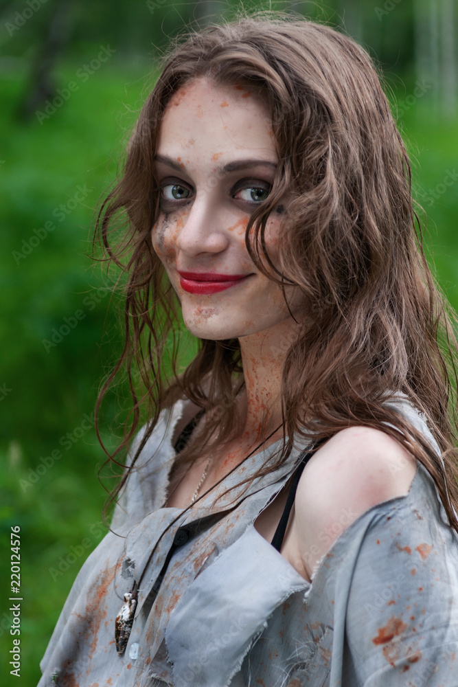 Beautiful young dirty smiling mad and manic looking girl wearing torn clothes and smeared with mud and dried blood stands in the forest. Beautiful young dirty smiling mad and manic looking girl wearing torn clothes and smeared with mud and dried blood stands in the forest.