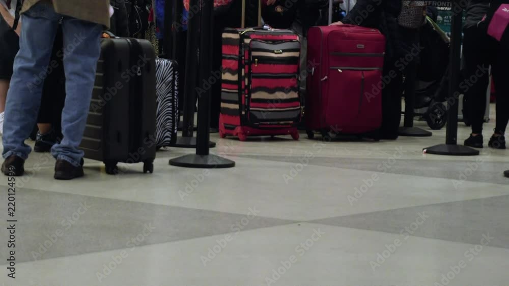 View of peoples legs as they wait in line at an airport terminal, and walk by with their luggage