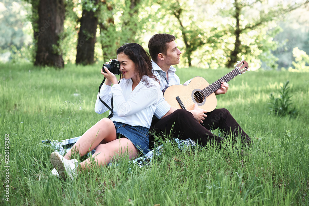 young couple walking in the forest and playing guitar, taking photo on old camera, summer nature, bright sunlight, shadows and green leaves, romantic feelings young couple walking in the forest and playing guitar, taking photo on old camera, summer nature, bright sunlight, shadows and green leaves, romantic feelings