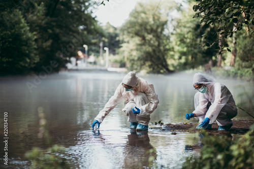 Two scientists in protective suits taking water samples from the river. photo