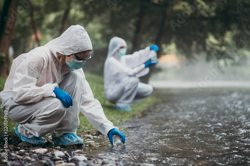 Murais de parede Two scientists in protective suits taking water samples from the river