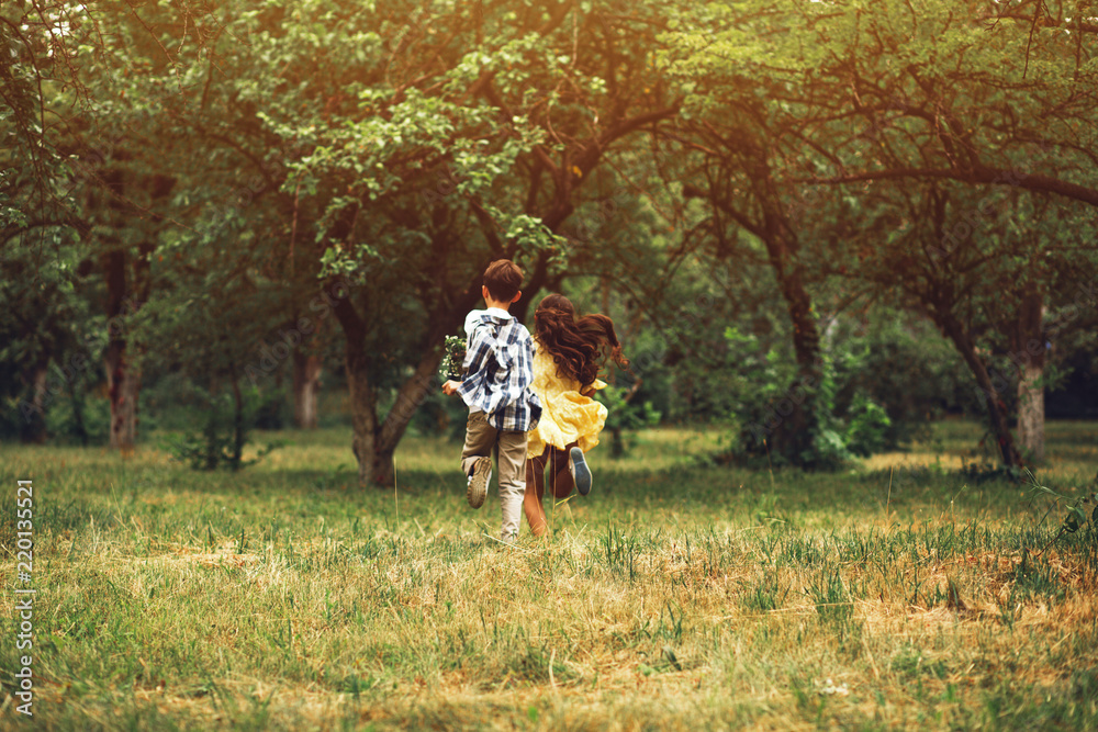 Boy and girl running in distance holding hands. Romantic little couple of sweet children running away into nature holding hands together.