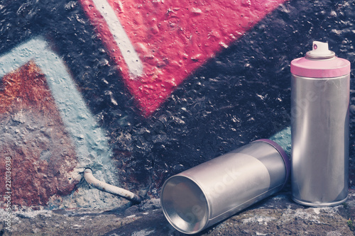 Several spray cans with paint and caps for spraying paint under pressure is lies near the painted wall in colored graffiti drawings