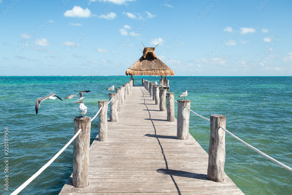 Fototapeta premium Ocean view from a pier with seagulls perched on either side of it and a grass roof at the end.