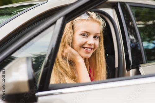 Blond teenage girl sit in car and smile