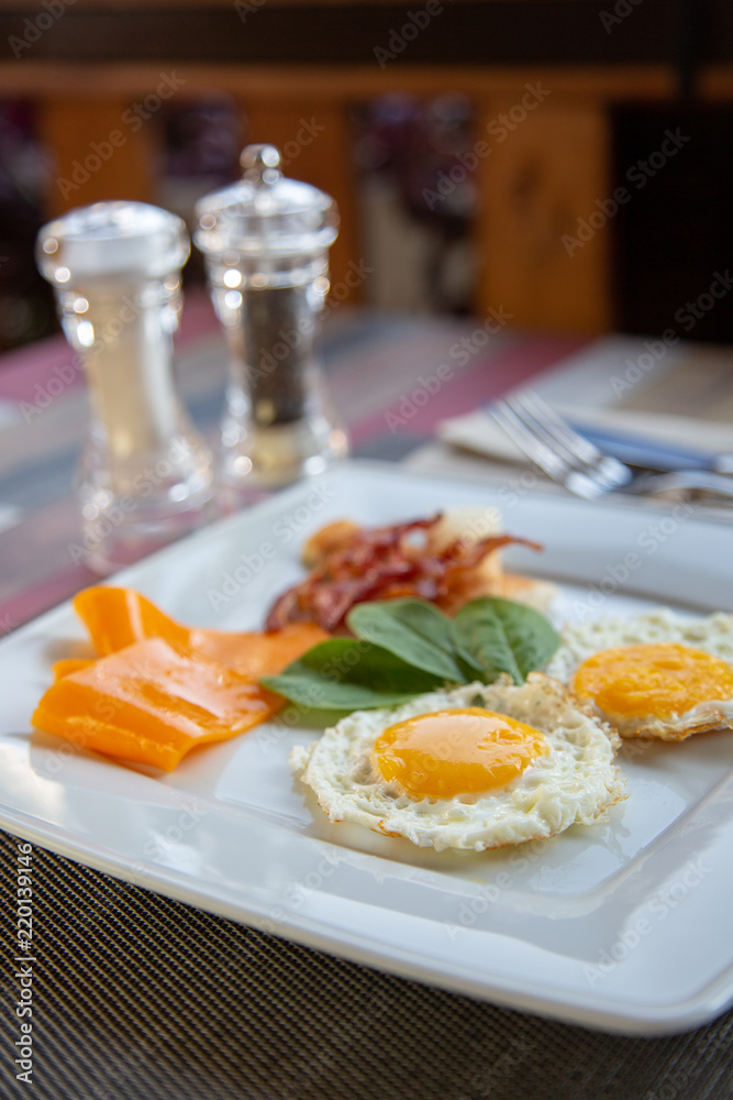plate of fried eggs with bacon and vegetables on dark background, top view