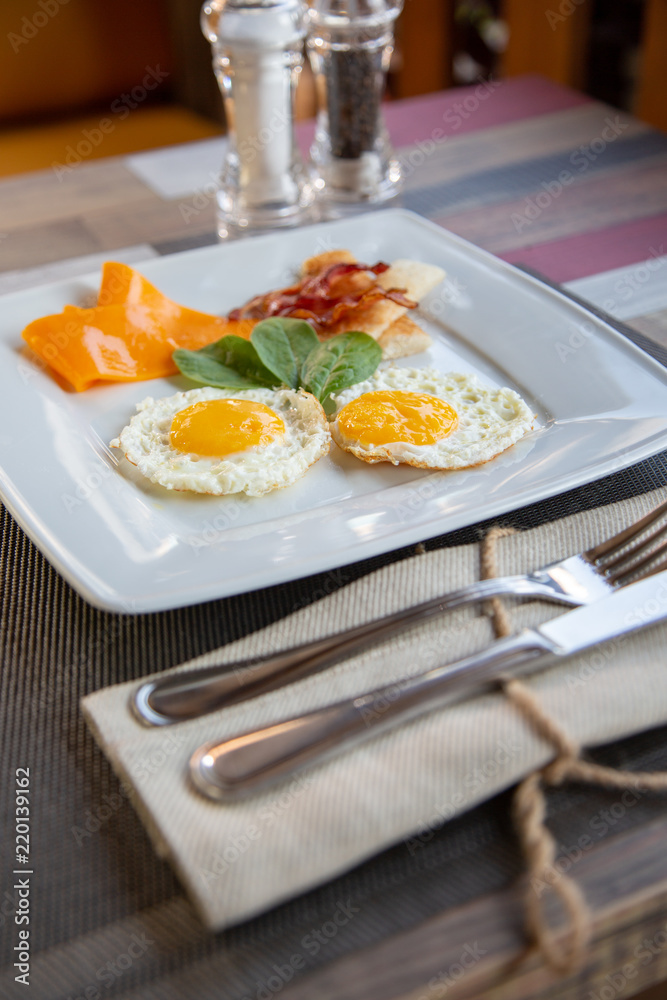 plate of fried eggs with bacon and vegetables on dark background, top view