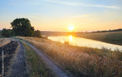 Sunny summer landscape with ground country road river and rising sun.