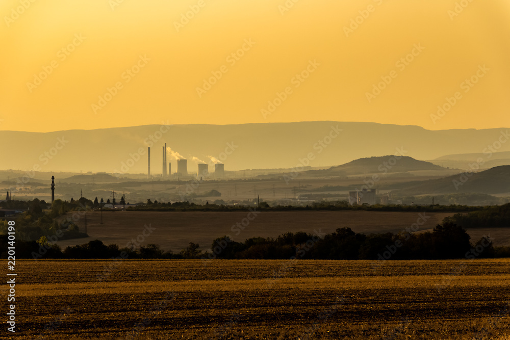 Factory with chimneys and cooling towers in the landscape during sunset