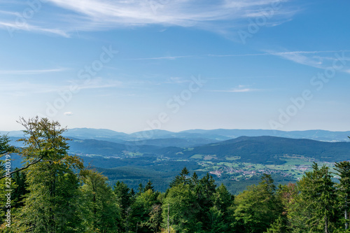 View from top of a mountain in the valley with clouds on the sky and mountains on the background and trees in front of in the bavarian forest
