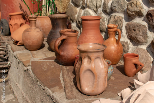 Many ceramic handmade utensils on stone shelf outdoor.