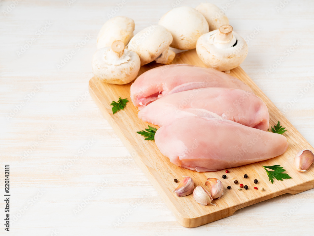 raw chicken breast fillet with spices on a wooden board on white wooden table, side view, copy space